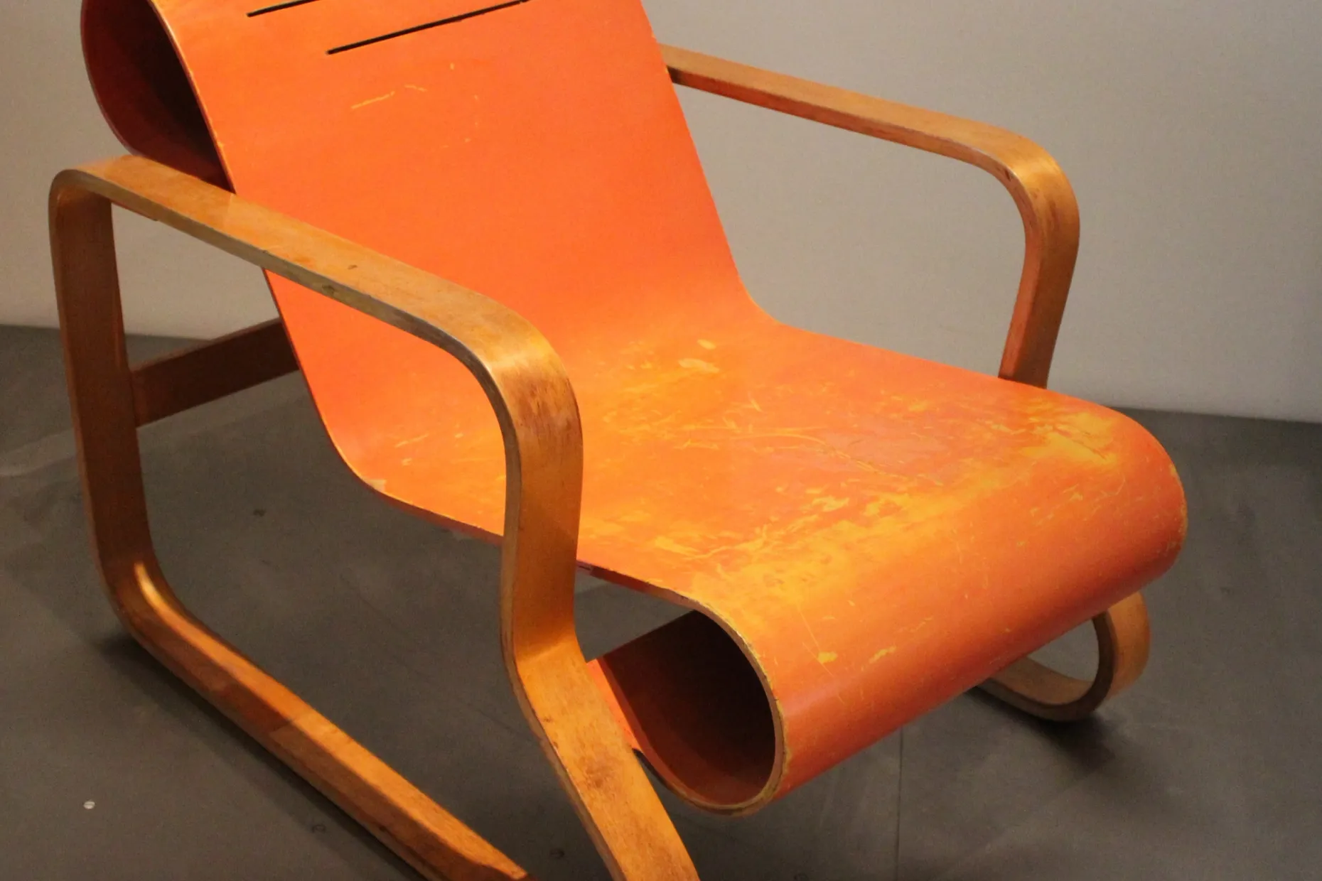 Orange bent plywood Paimio armchair by Alvar Aalto on a museum floor