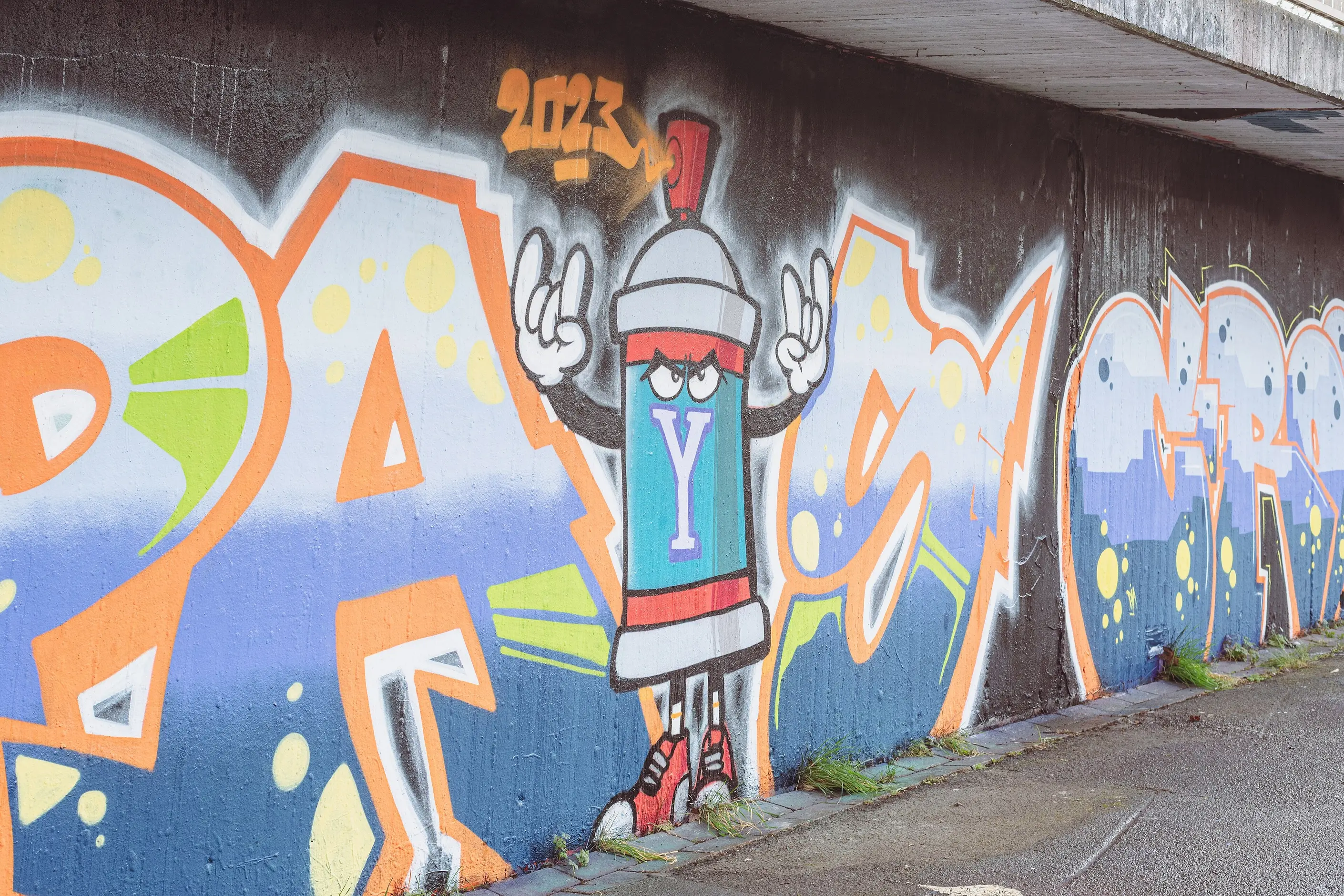 Large graffiti mural of interlocking block letters and a cartoon spray can character