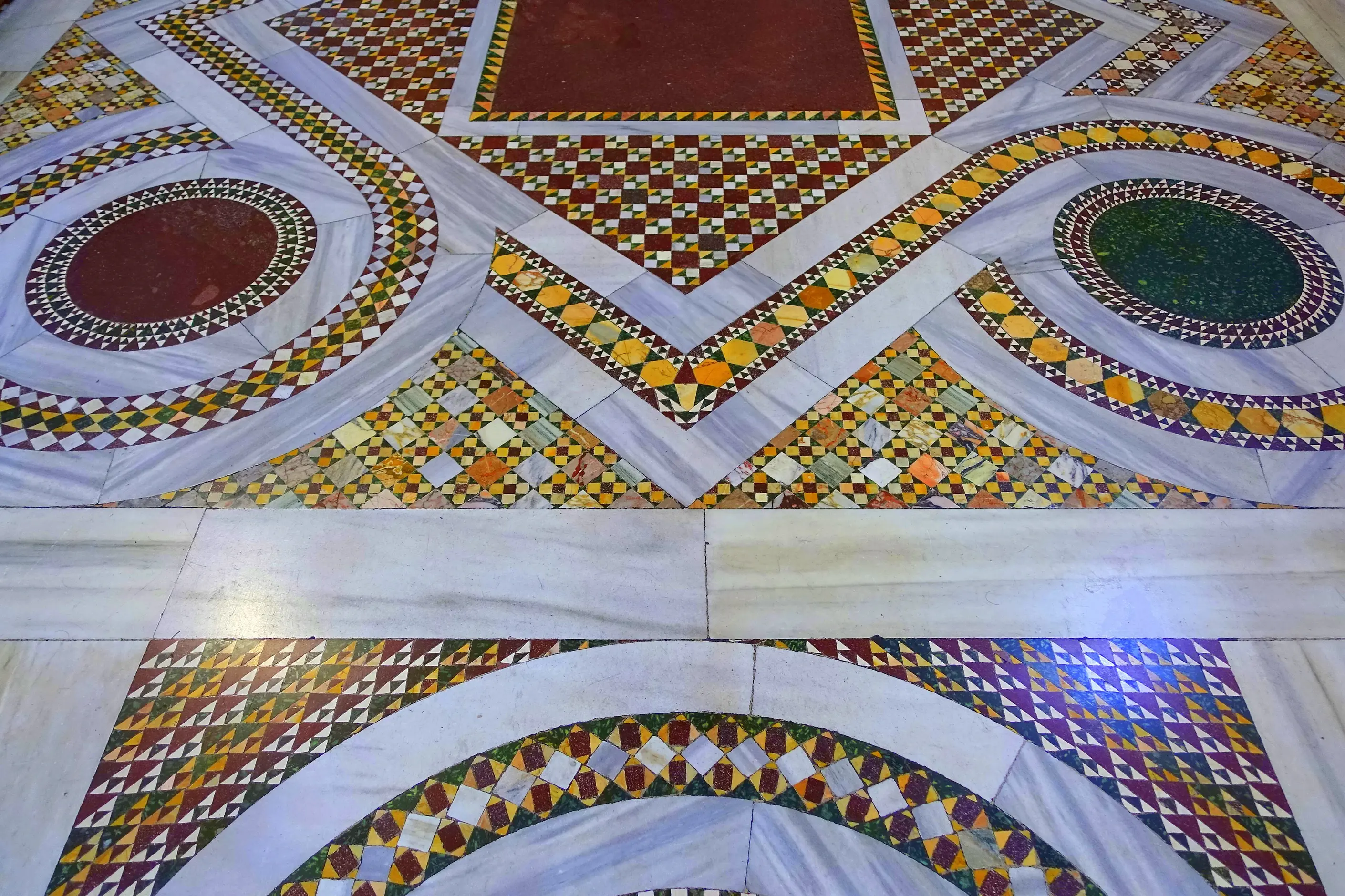 A Cosmatesque marble floor of red and green roundels framed by bands of tiny triangular and square tiles