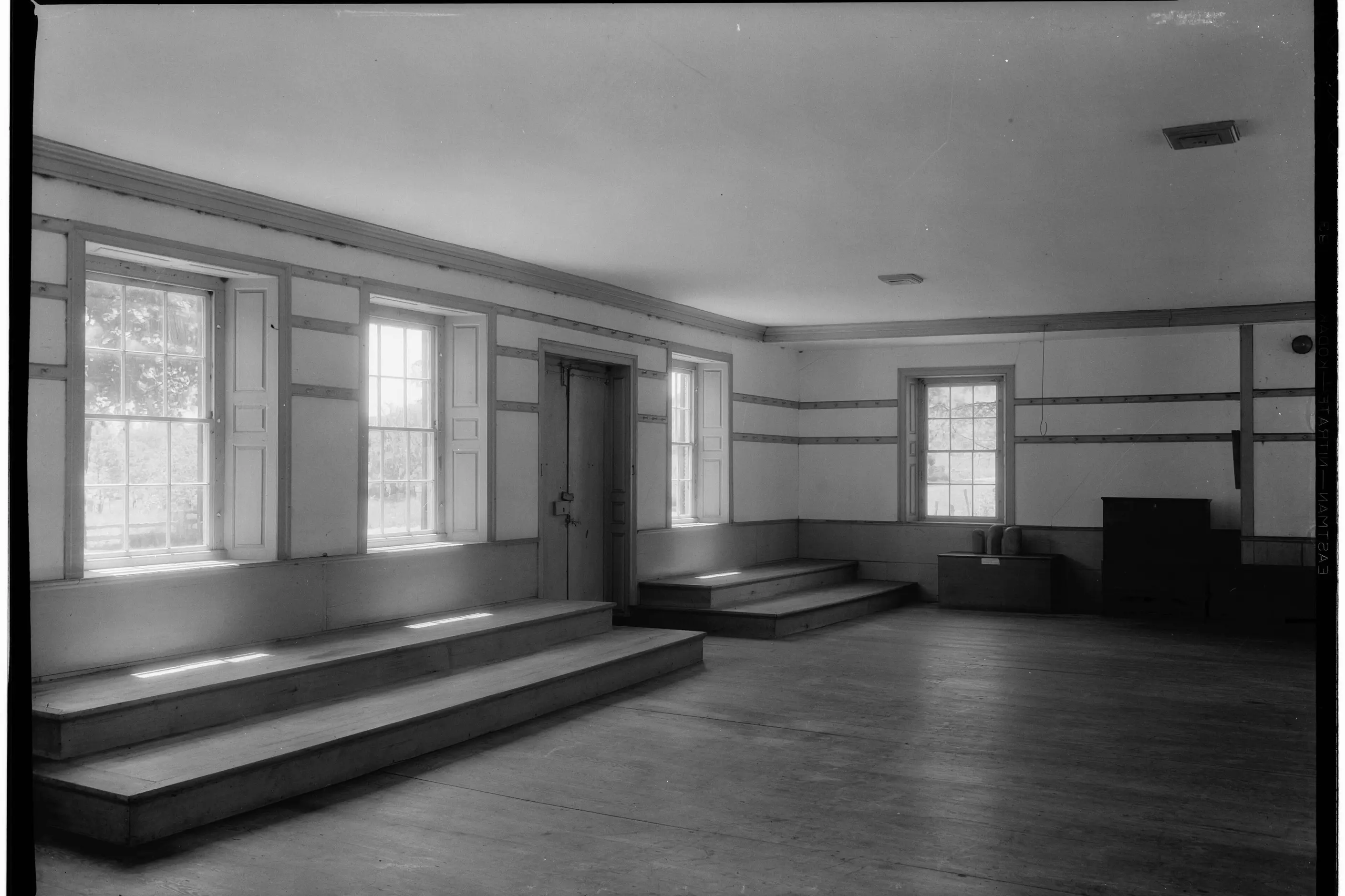 Plain Shaker meeting room with tall windows, a raised platform and bare wood floor