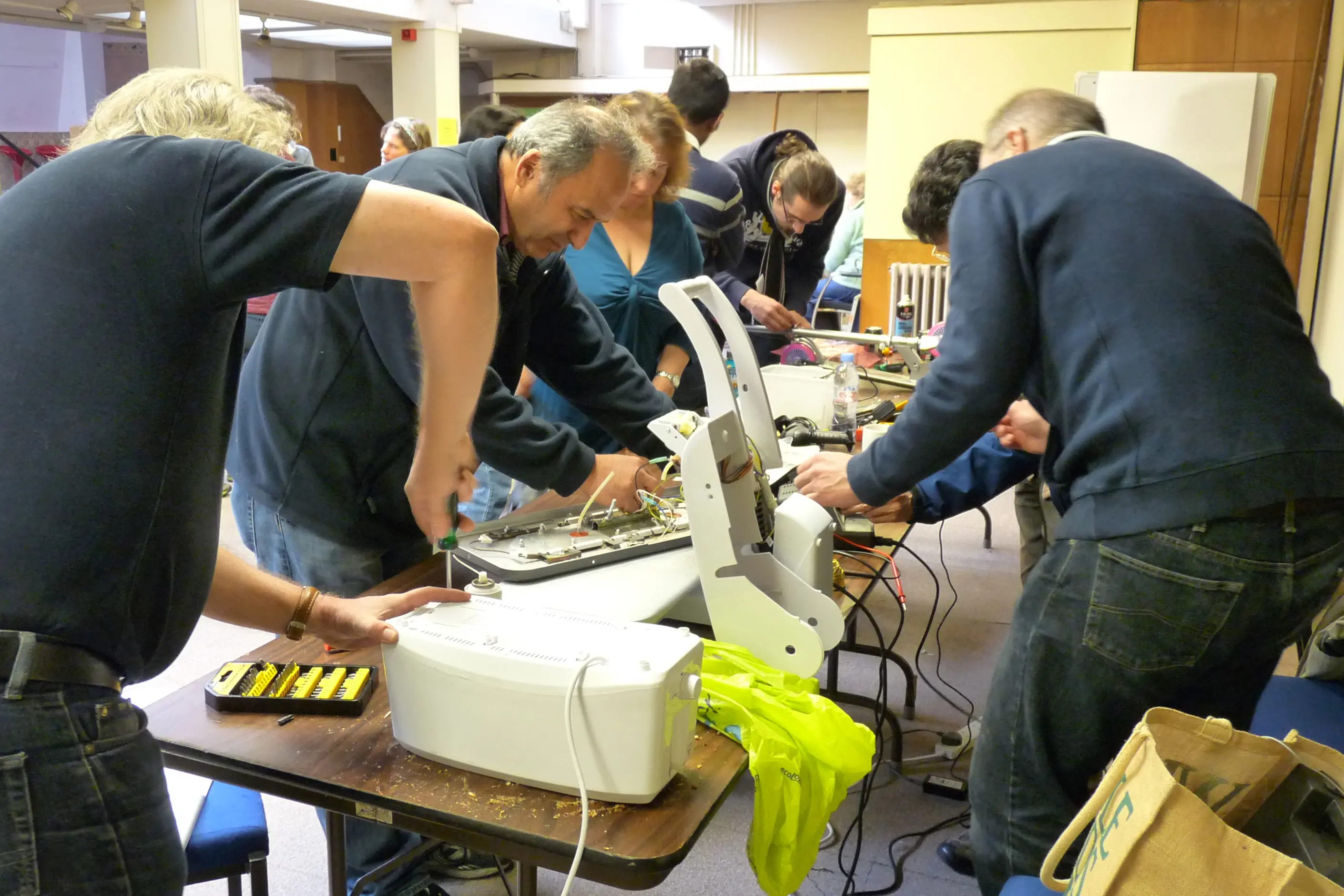 Volunteers at a repair cafe bent over tables fixing a printer and small appliances