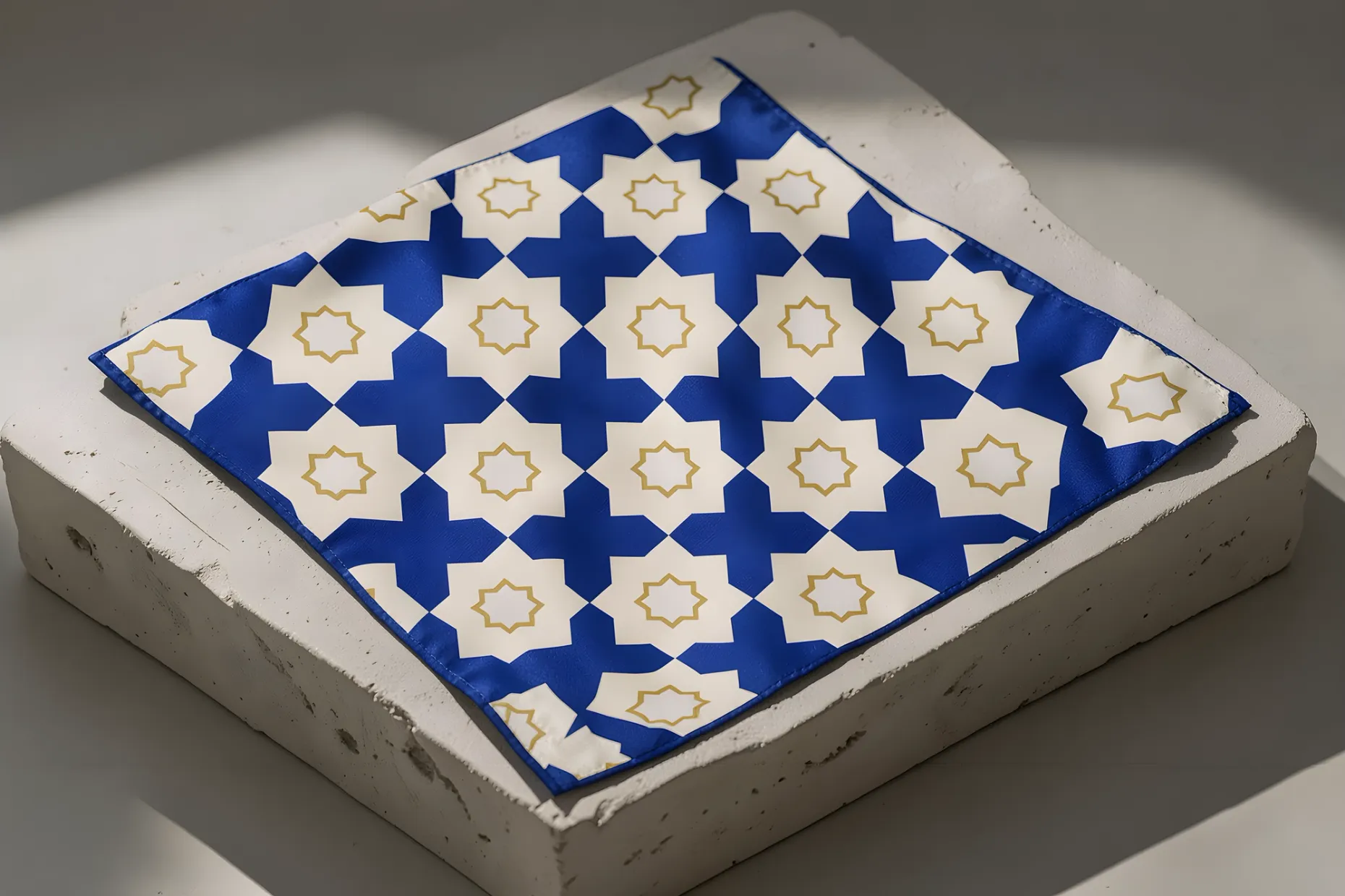 Silk scarf laid flat on a plaster plinth, printed with an eight-fold star and cross pattern in cobalt, ivory and gold