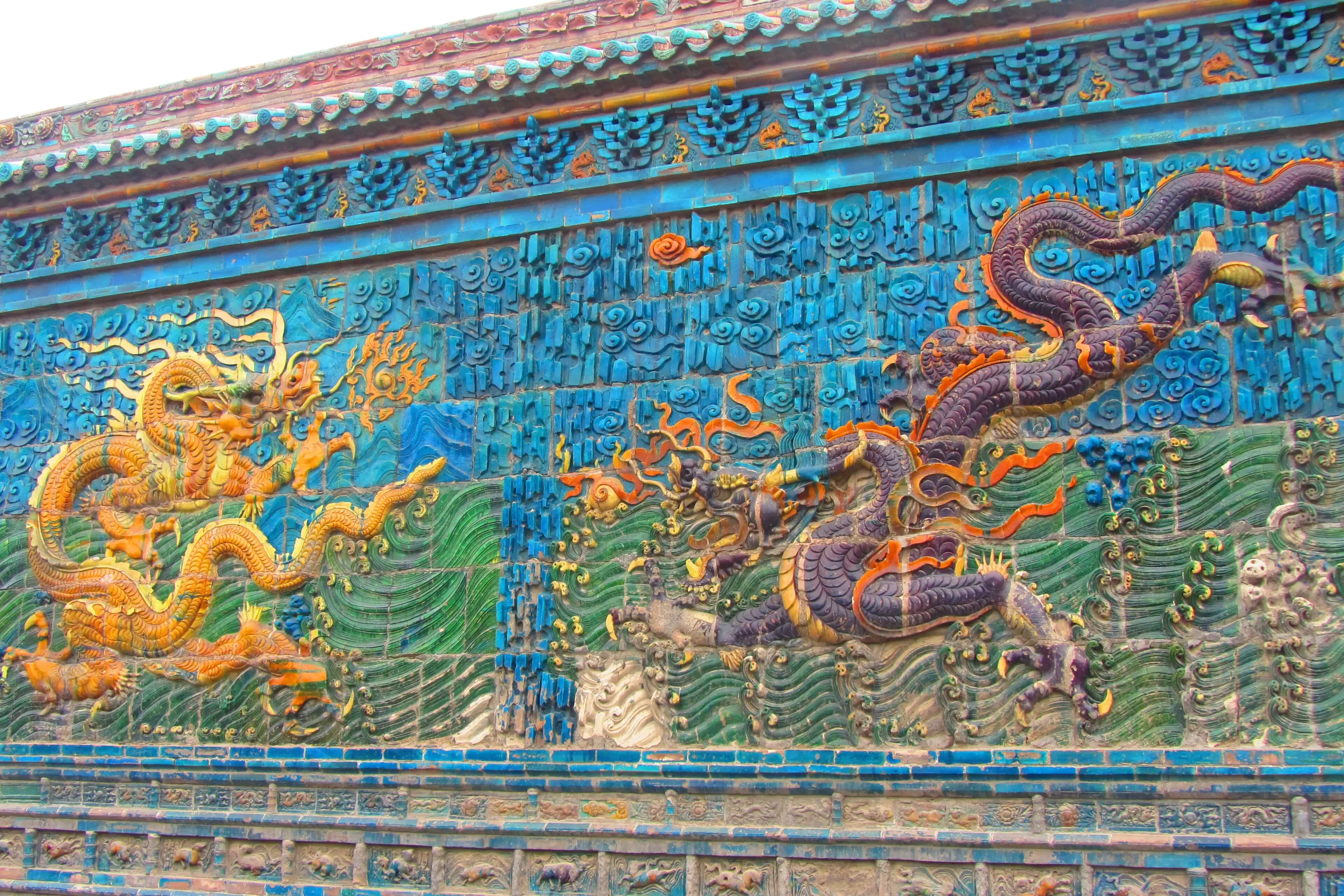 Glazed ceramic dragons, one yellow and one purple, writhing across a turquoise tiled wall of waves and clouds