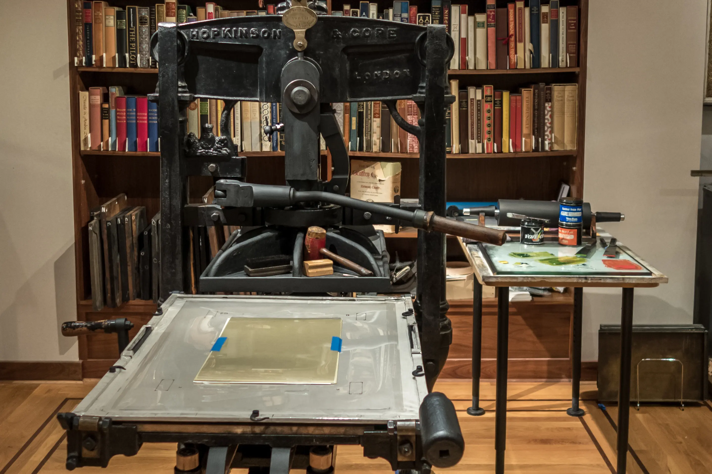 A black cast-iron Albion hand press in a book-lined room, the kind the Kelmscott Press printed on