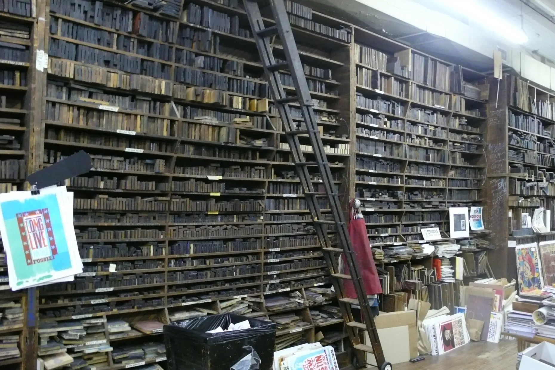 A print shop crammed floor to ceiling with shelves of wood type and printing blocks, posters pinned by the door
