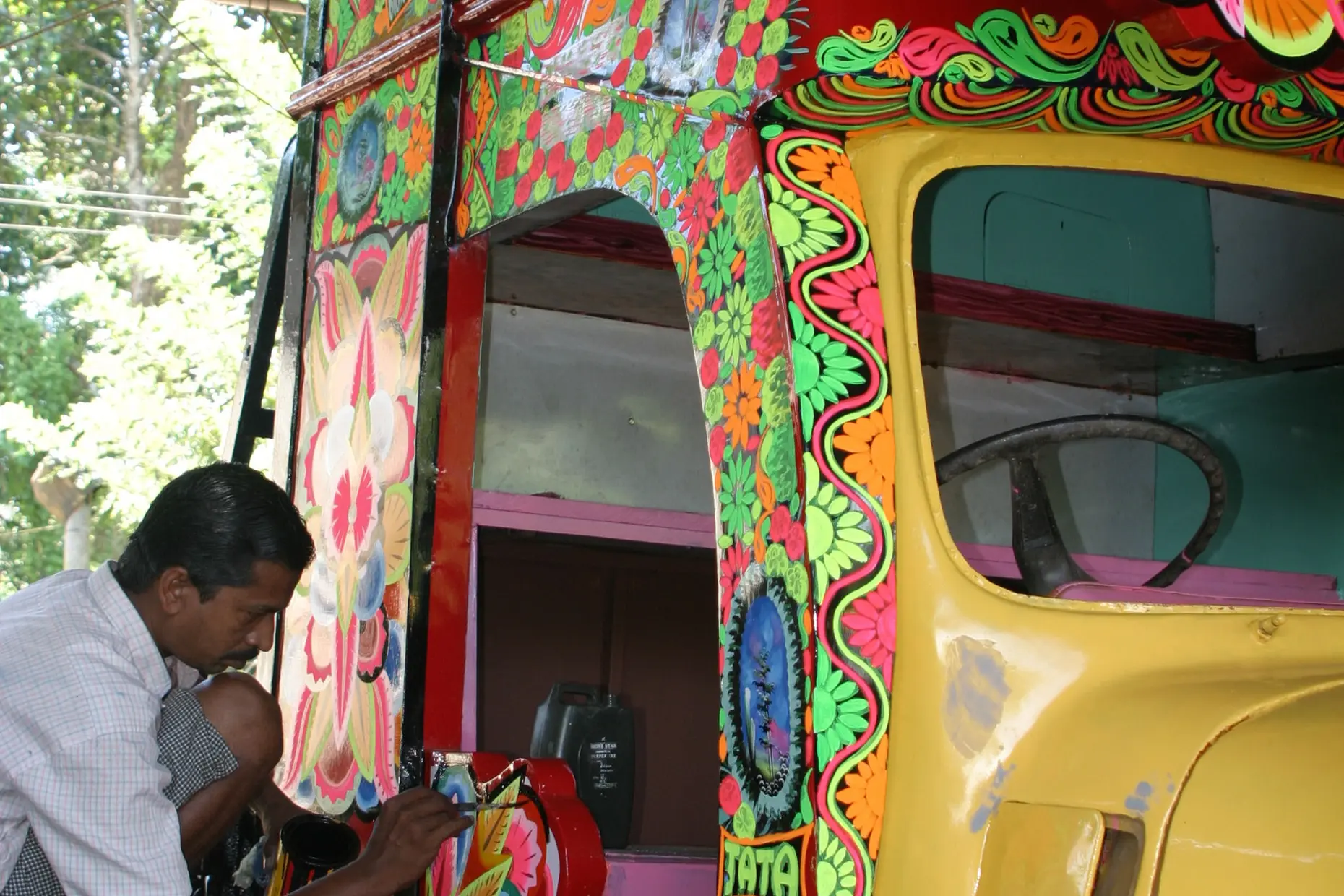 Painter hand painting floral patterns on a decorated truck cab near Cochin, India