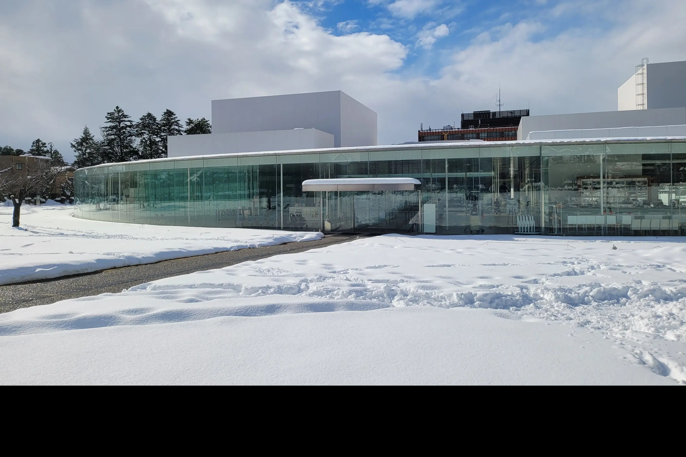 Circular glass walled museum building with a curved facade seen across snow