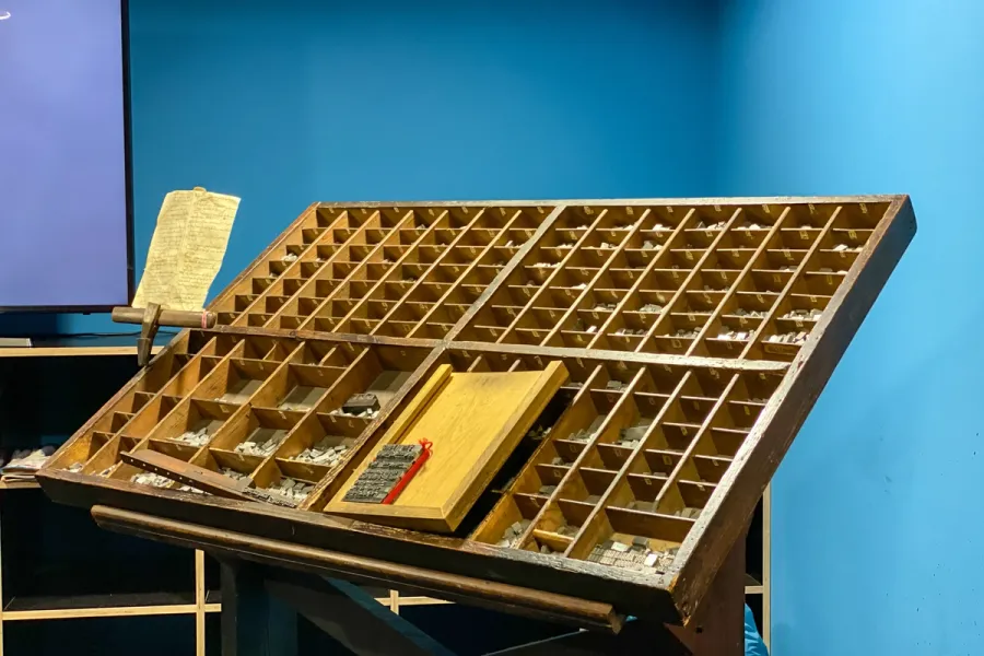 Wooden type case tilted on a stand holding metal letterpress sorts and a manuscript