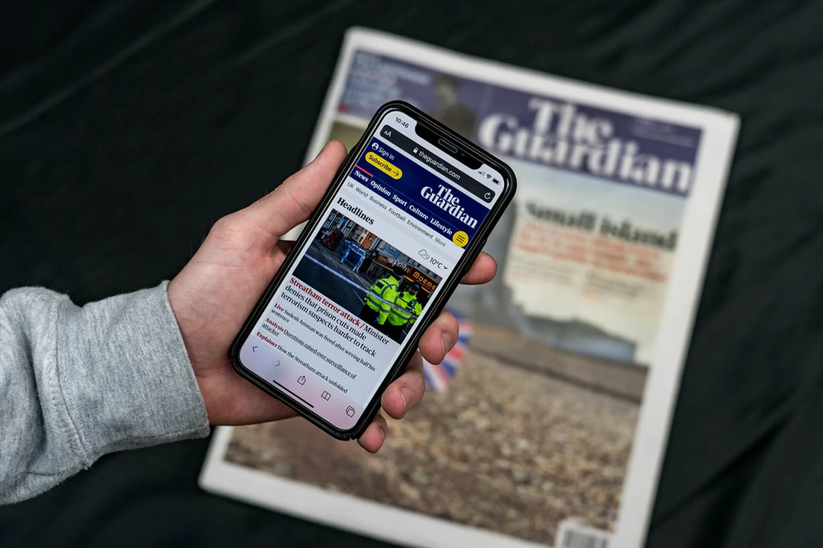 A hand holding a phone showing The Guardian's app over a printed copy of The Guardian newspaper