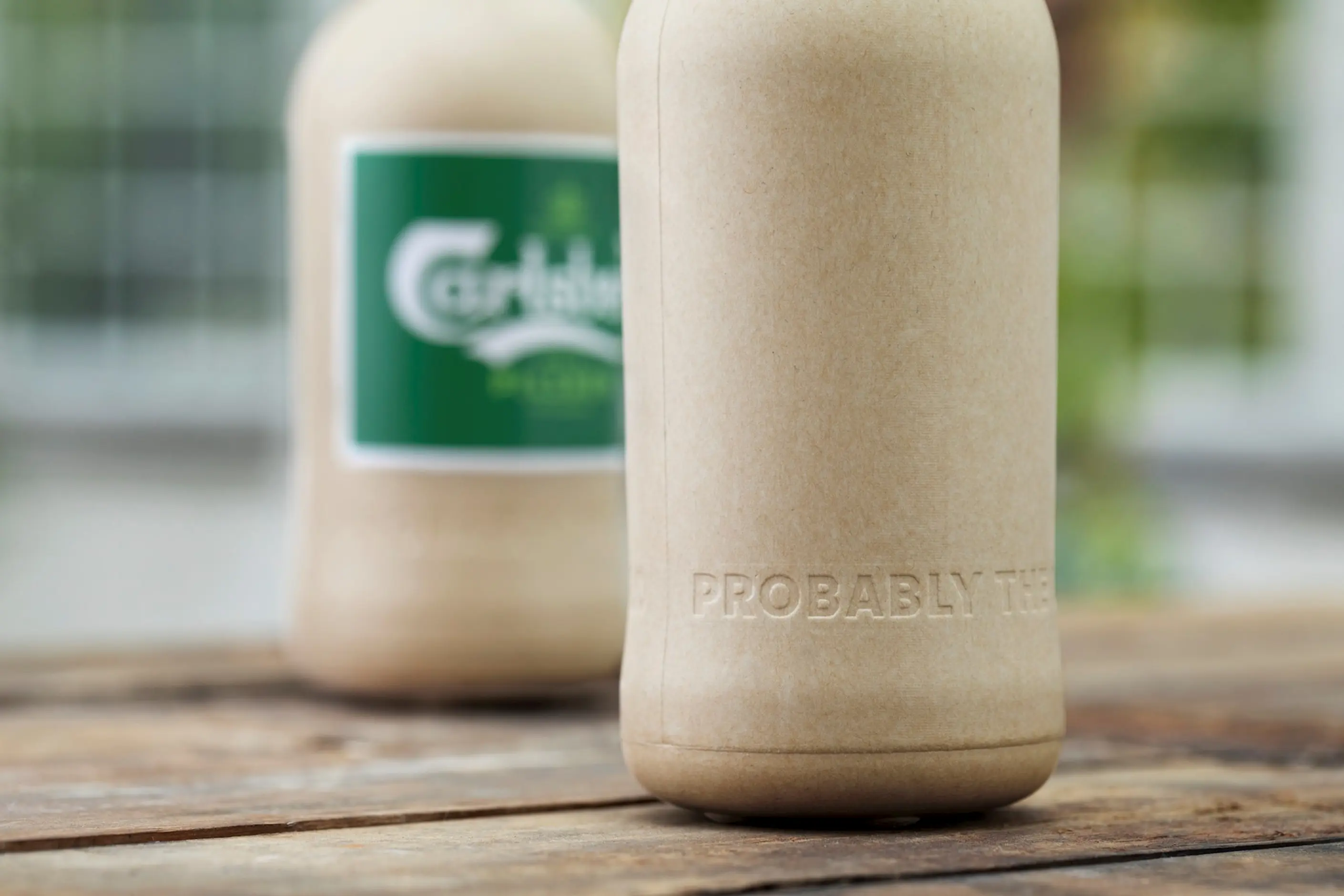 A wood fibre Carlsberg beer bottle prototype beside a standard glass Carlsberg bottle
