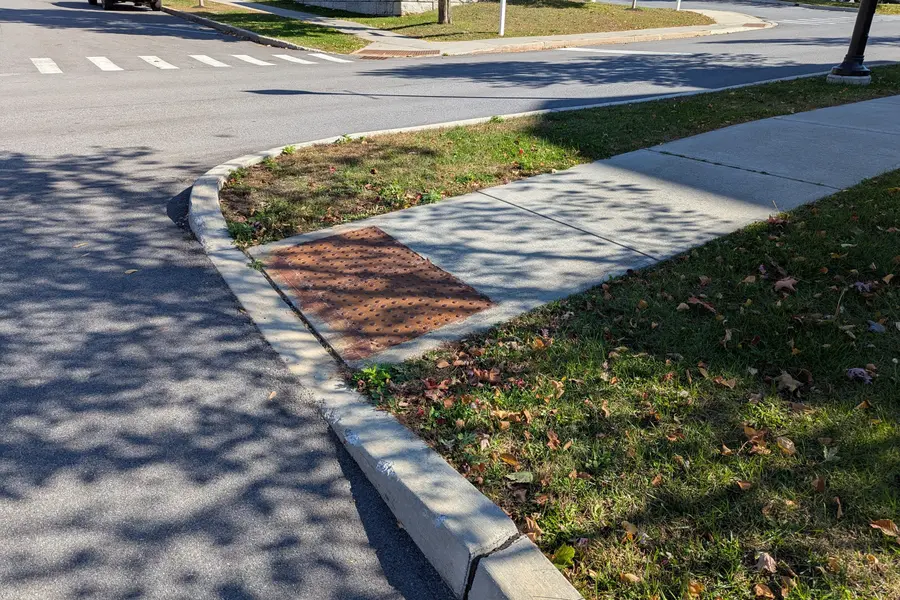 Curved curb cut ramp with tactile paving at a suburban street corner