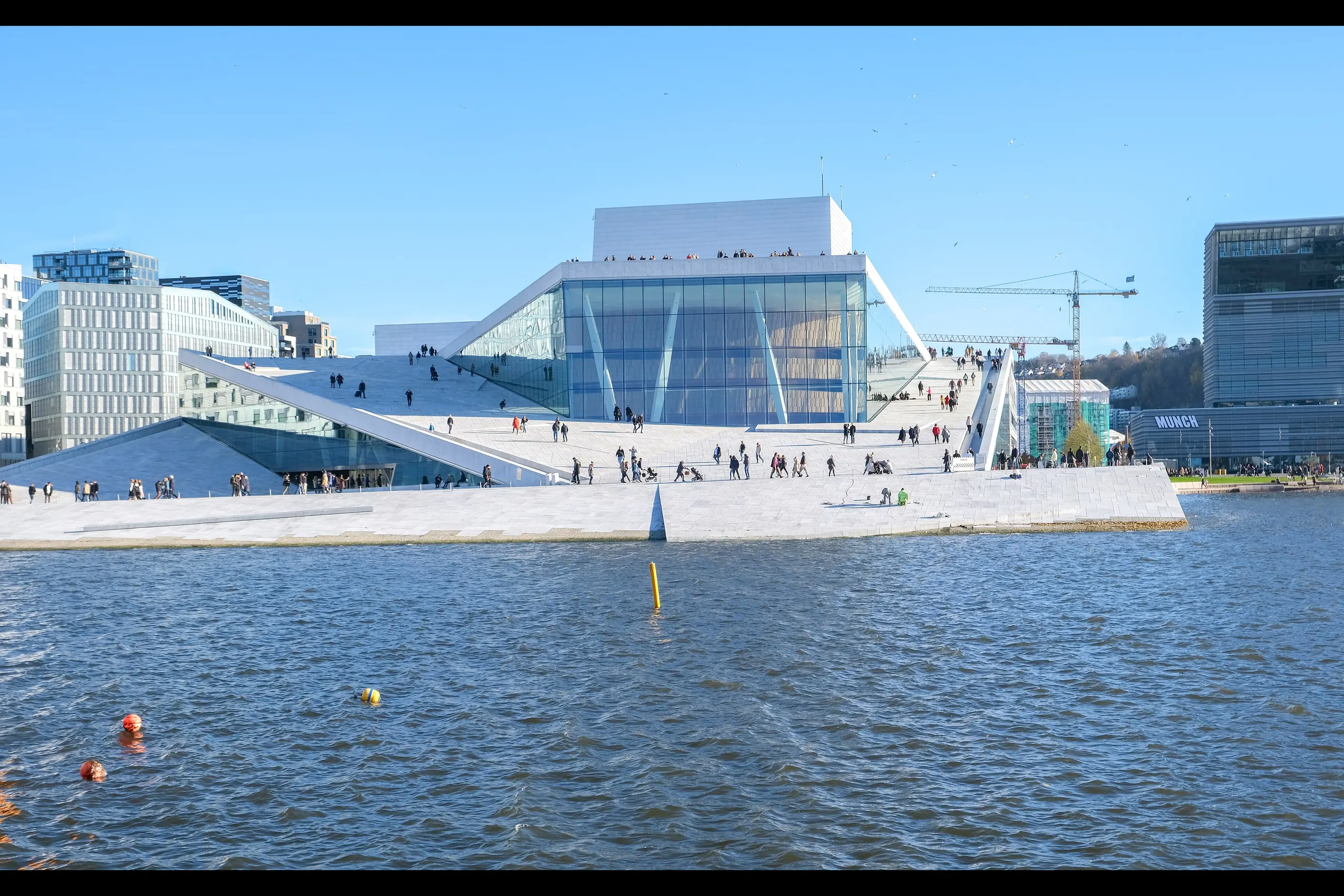 Oslo Opera House by Snøhetta, its white marble roof sloping into the harbour with people walking on it
