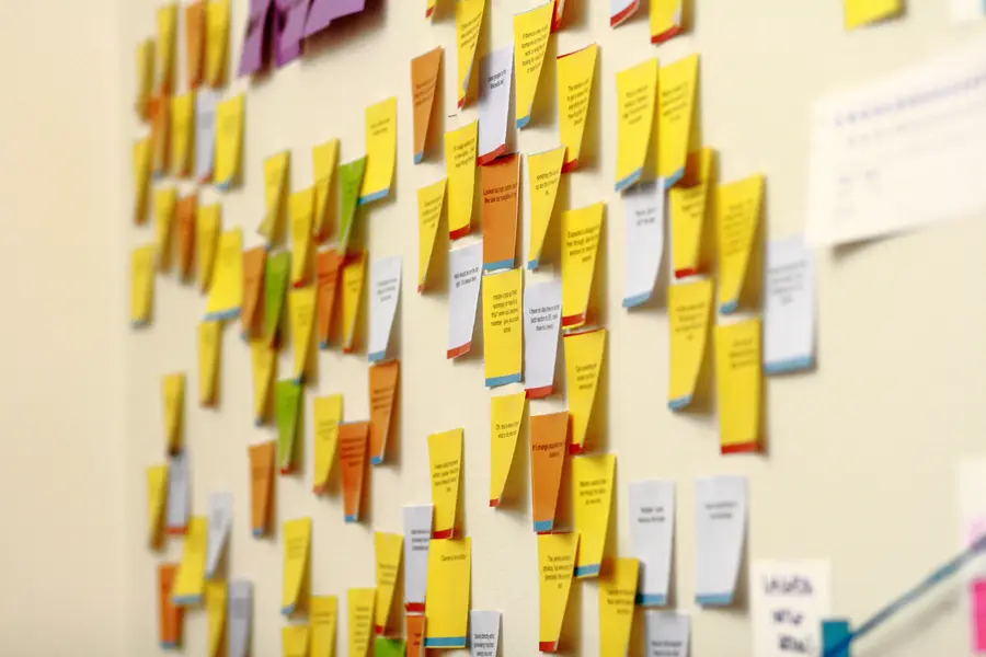 A wall covered in rows of colour coded sticky notes with handwritten feedback, sorted into columns