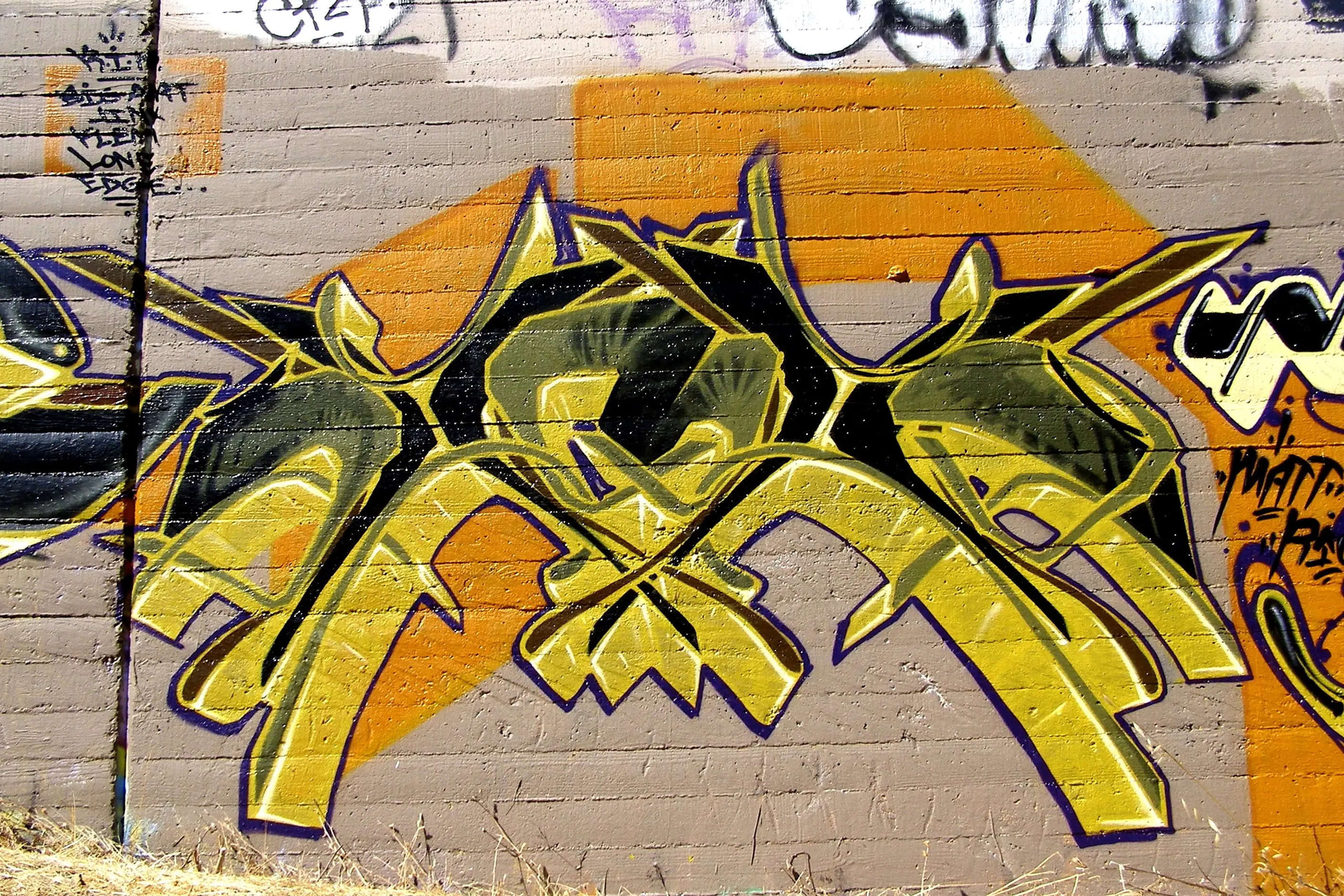 Interlocking yellow wildstyle graffiti letters with arrows on a wall