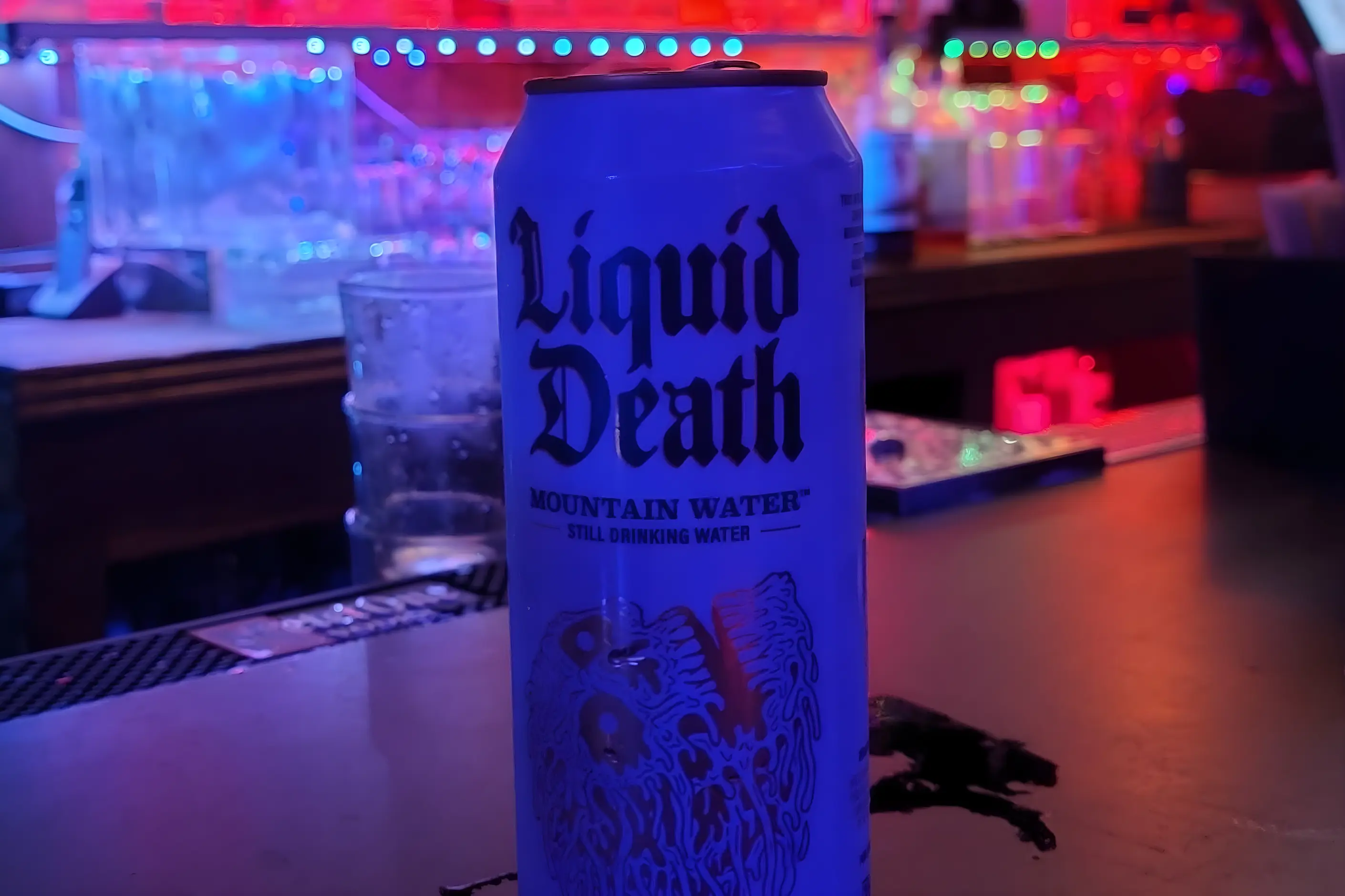 Liquid Death Mountain Water can with gothic lettering on a neon lit bar counter