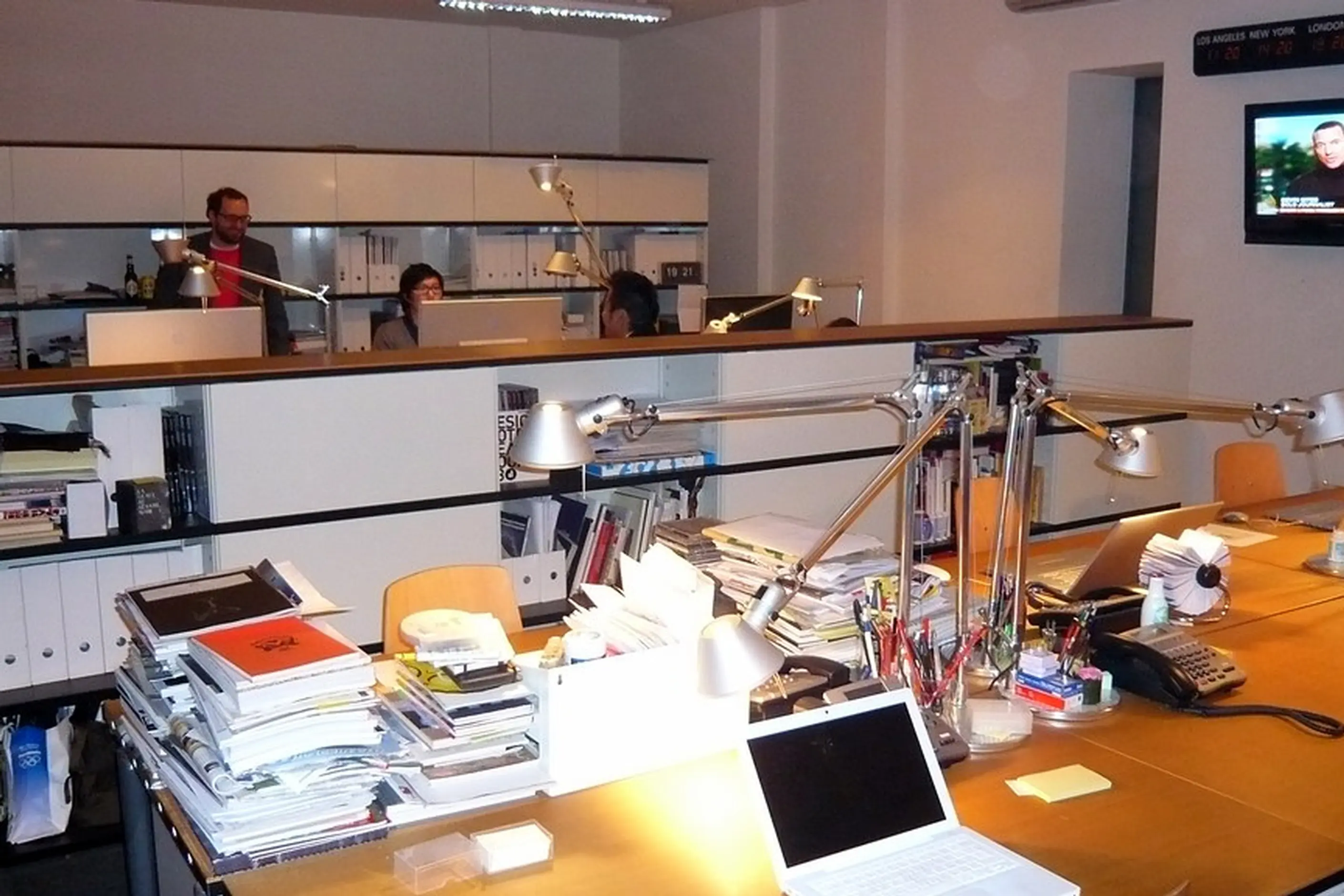The Monocle editorial office: long shared desks stacked with proofs and back issues under task lamps, editors at work