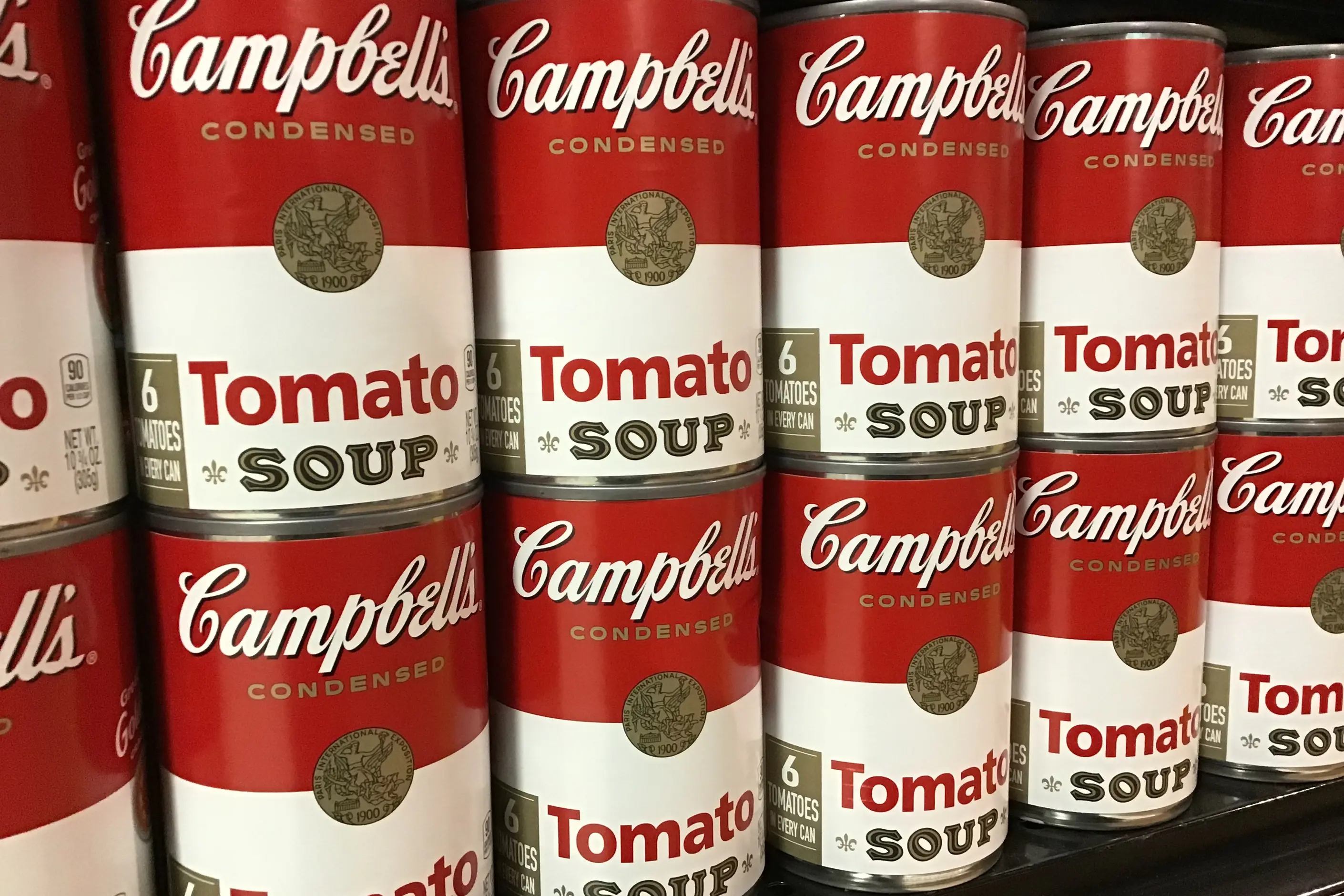 Rows of identical Campbell's Condensed Tomato Soup cans stacked on a store shelf