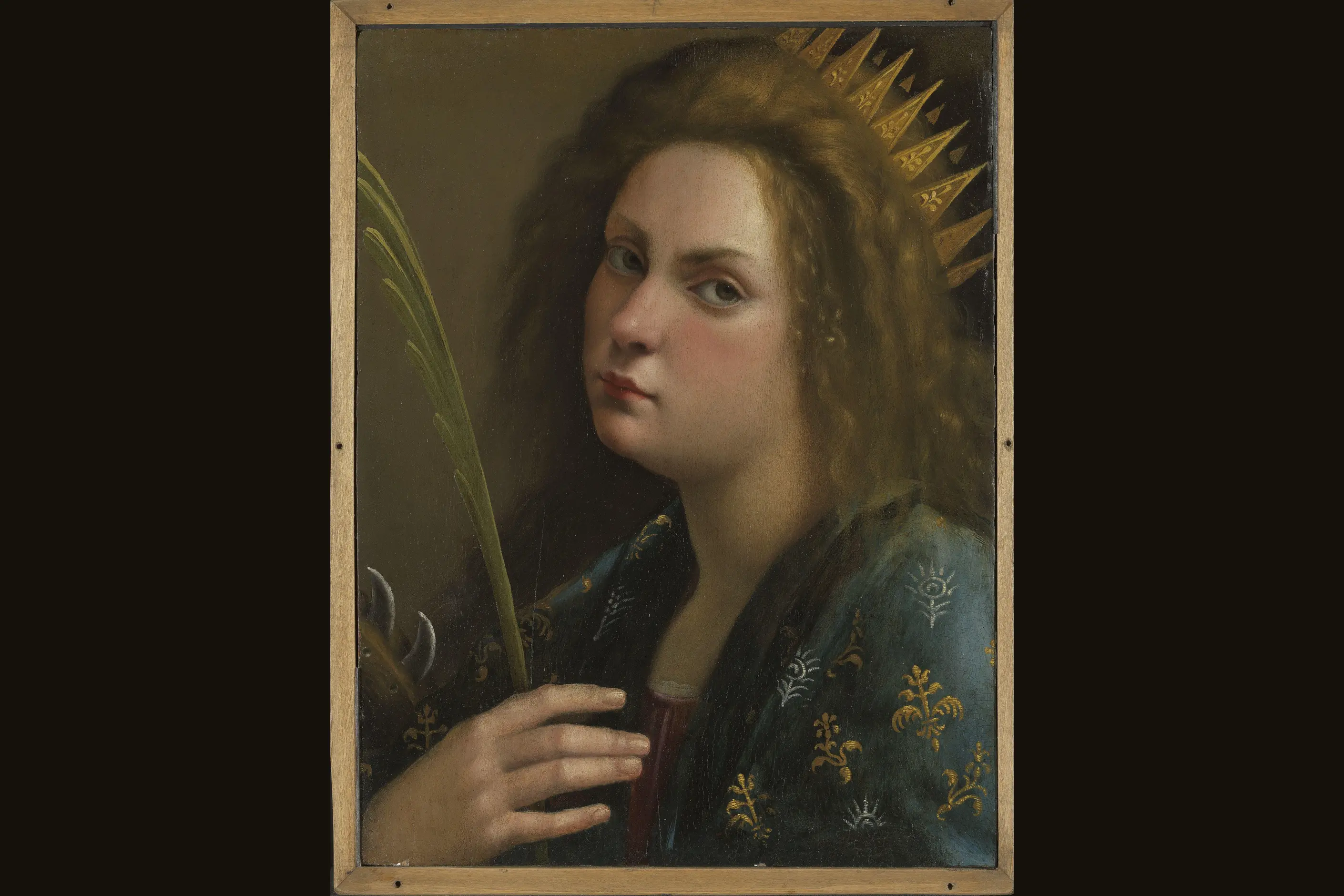 Portrait of a woman with a gold spiked halo holding a palm frond against a dark background
