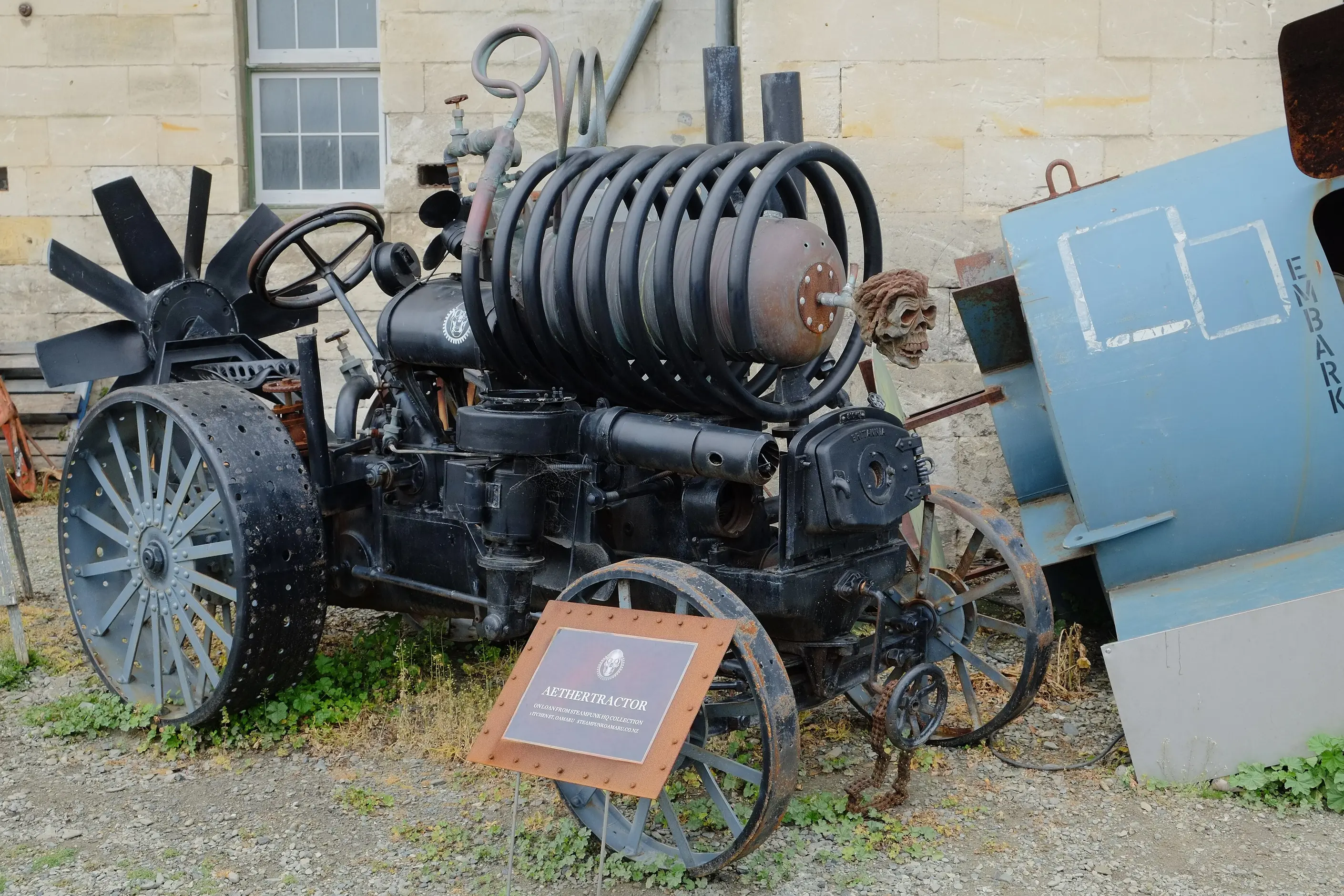 A black steampunk tractor with coiled pipes, fan blades and spoked iron wheels outside Steampunk HQ