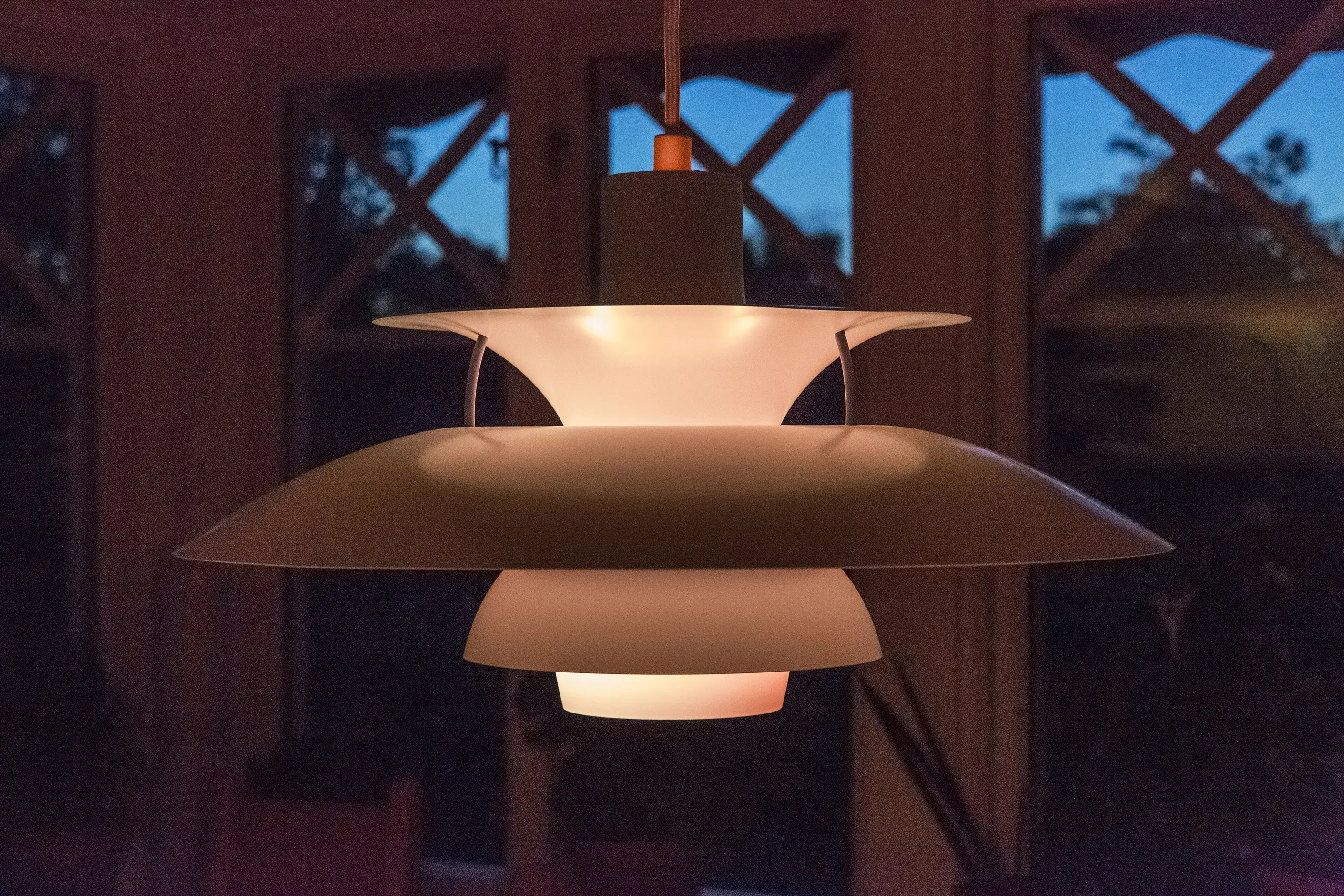 A layered PH pendant lamp glowing warmly against a darkening window