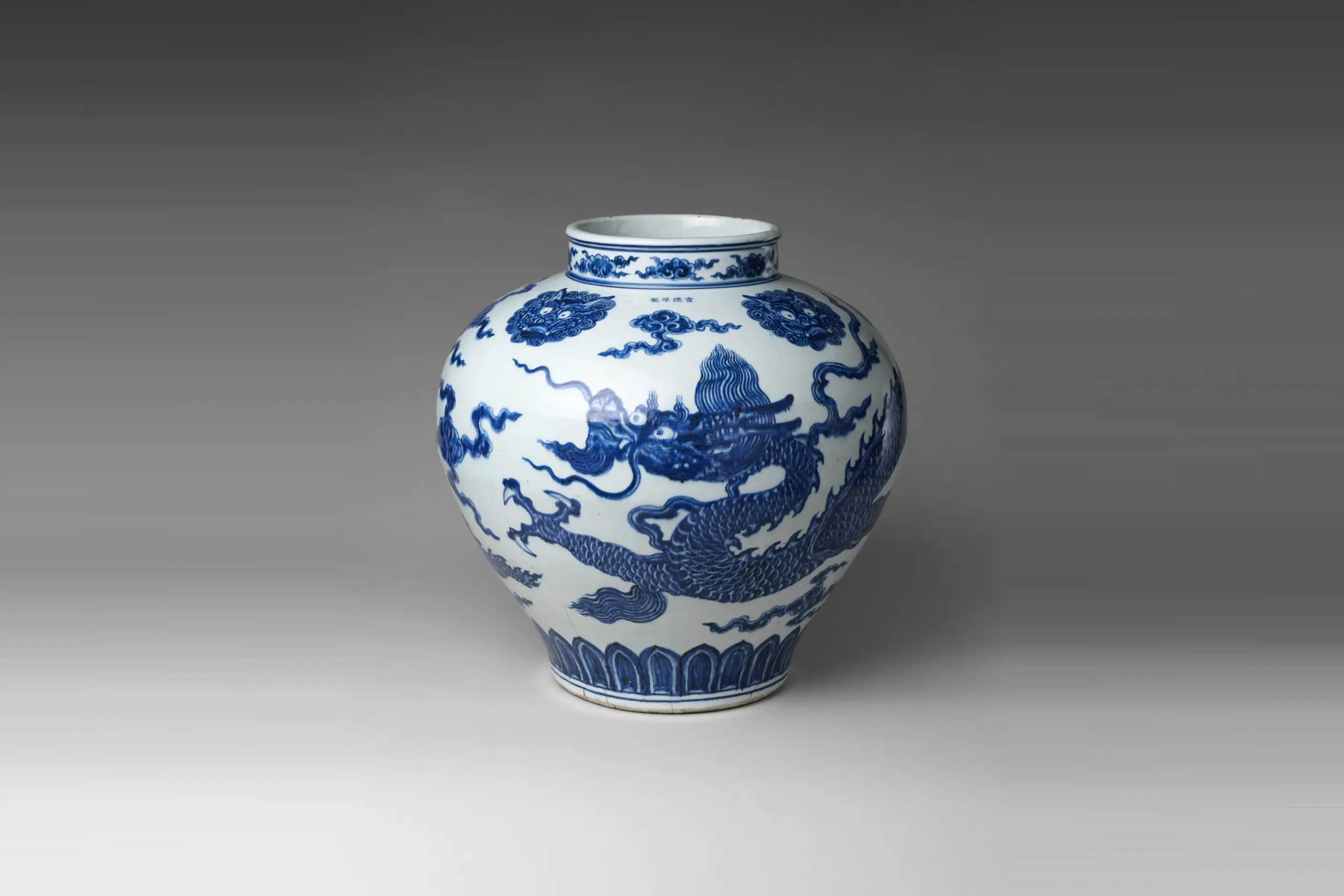 A Ming blue and white porcelain jar painted with a coiling dragon among clouds above a band of lotus petals