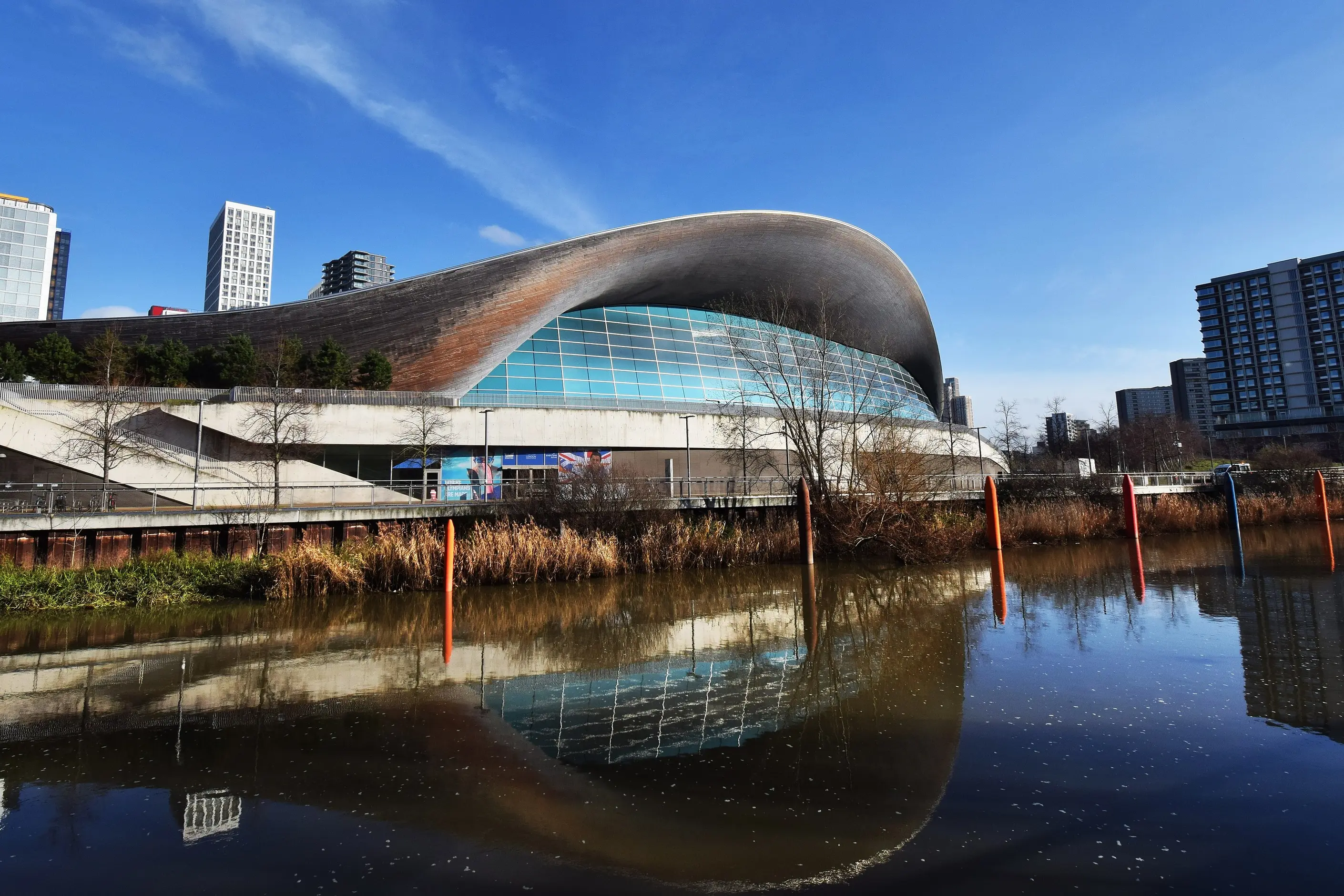 London Aquatics Centre's sweeping curved roof reflected in the water beside it